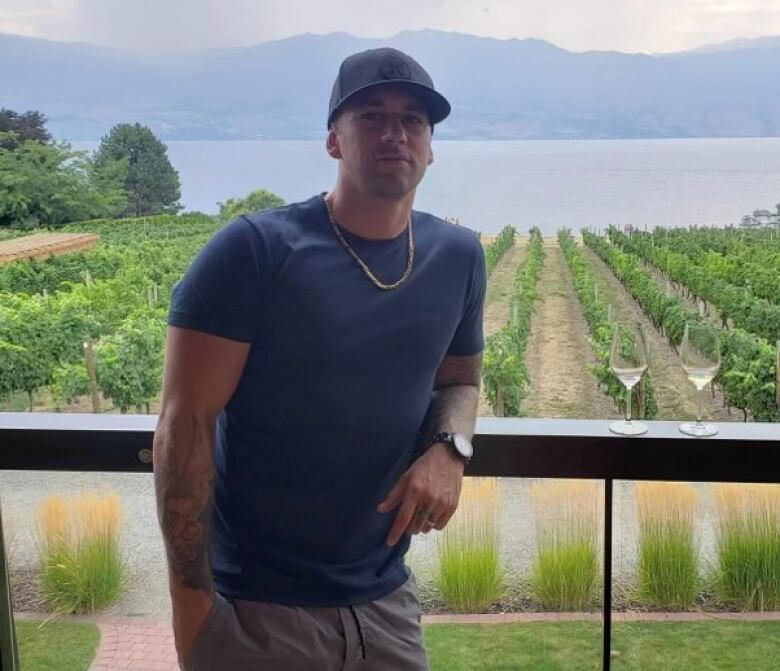 A man poses for a photo on a deck overlooking a vineyard.