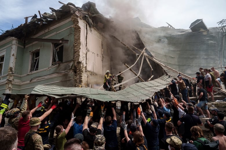 A large crowd of people hold up pieces of metal from a children's hospital that was hit by a missile in Ukraine. 