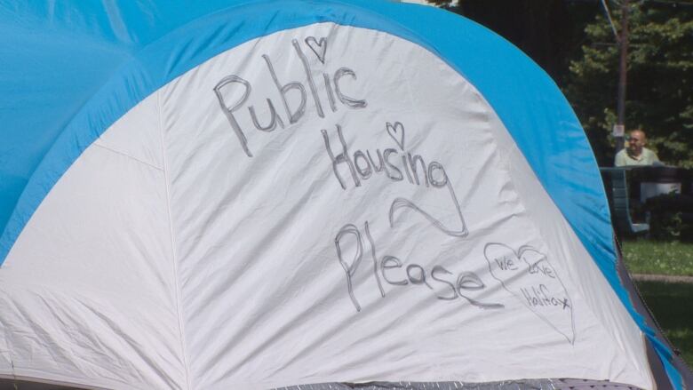 A white and blue tent has the words 'public housing please' written on its side