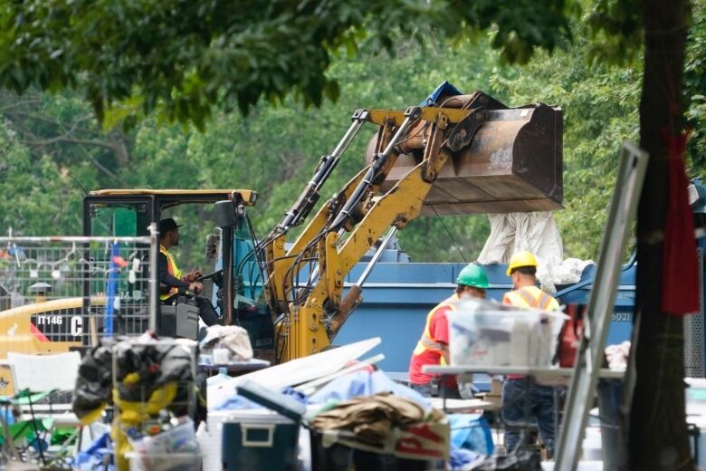 A frontloader throws a pile of debris away at an encampment. 