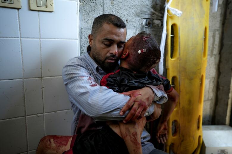 A man in a blue shirt holds a child in a red shirt in a hospital