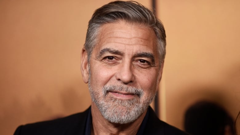 A handsome man with a grey beard smiles at the camera