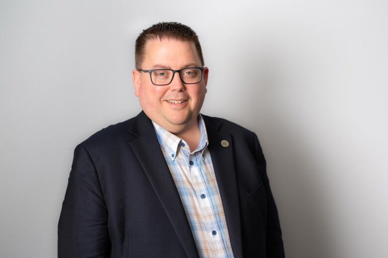 A man wearing a black blazer with a blue and yellow plaid shirt poses for a photo.