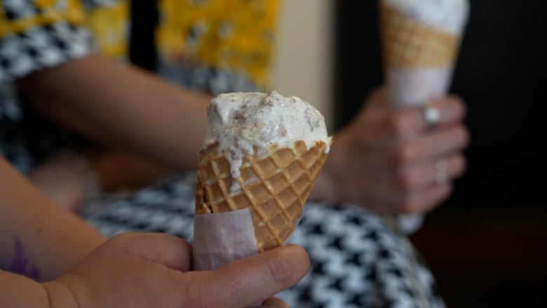 A hand holds an ice cream cone with a slowly melting white scoop 