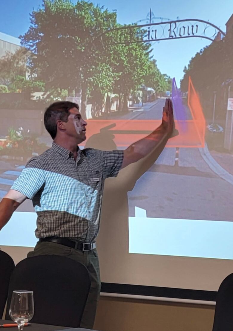 A man stands at a projector, pointing to a graphic of fencing, installed along Victoria Row. 