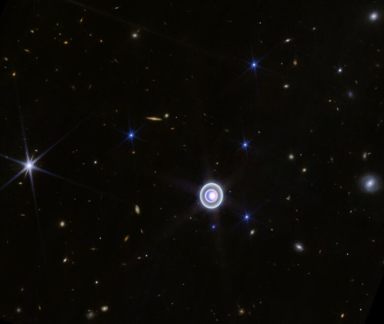 A ringed planet hangs in the blackness of space with stars and galaxies scattered around it.