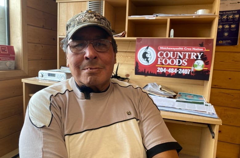 An elder wearing a ball cap sits in an office.