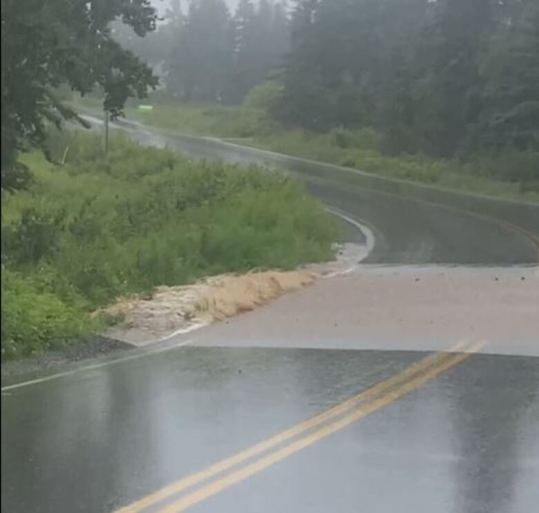 large pool of water over a stretch of road in the rain.