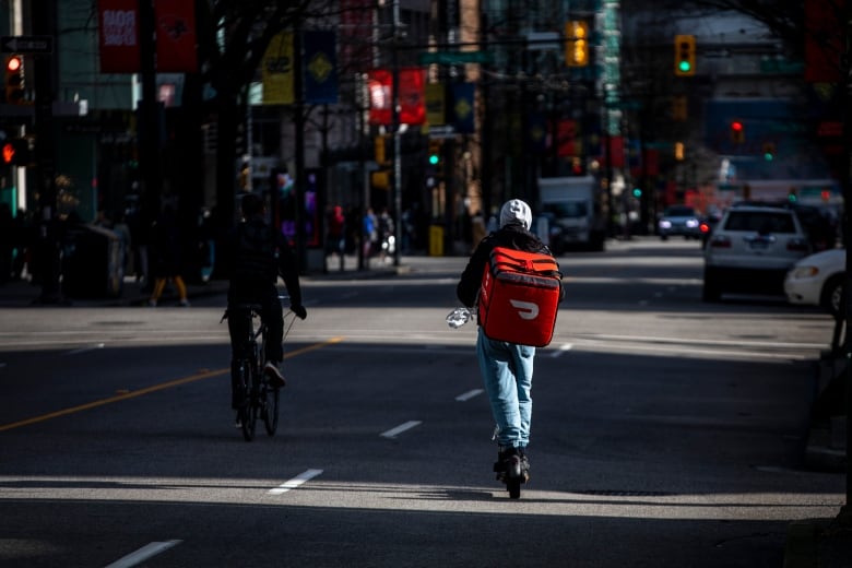 A person rides a kick scooter in downtown Vancouver. 