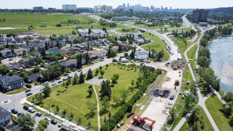 an aerial view of three sections of road with massive construction occurring. the city skyline and river are in the background.