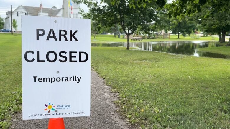 A white sign that reads, 'park closed temporarily,' in front of a flooded park. 