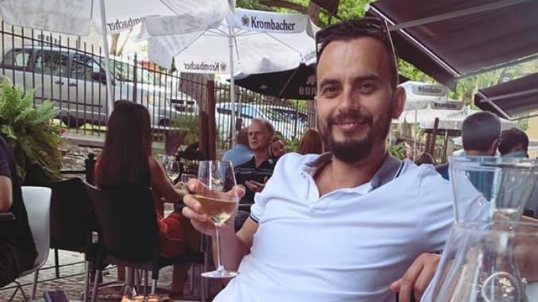 Nikolay Goltsev sits at a dinner table holding a glass of wine smiling at the camera.