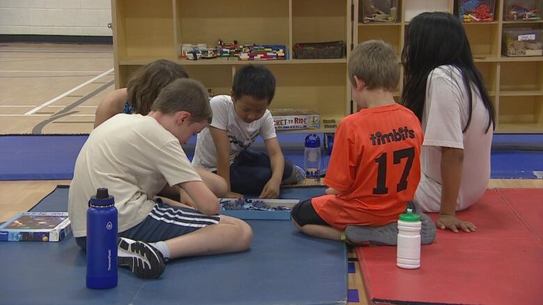 Five children sit at a mat on a school gym, playing a board game