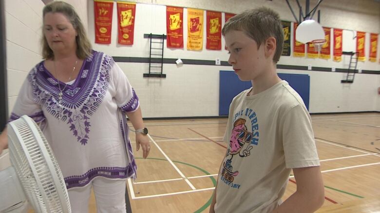 Child stands in front of a fan inside a school gym