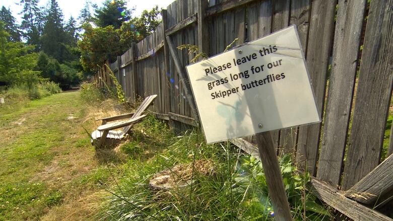 A sign posted outdoors reads 'Please leave this grass long for our Skipper butterflies.