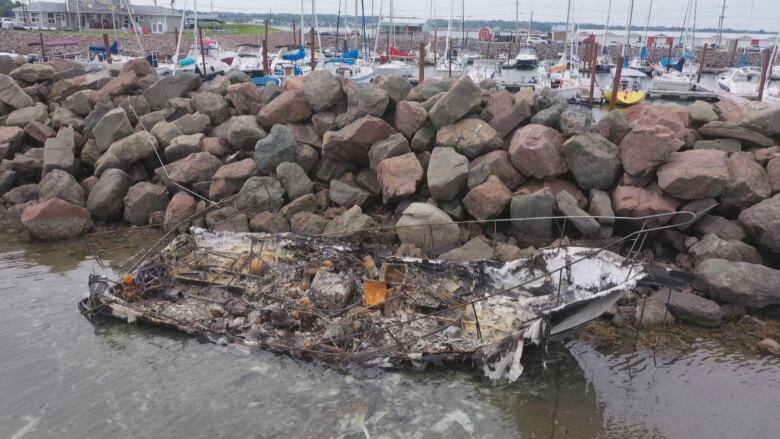 The charred remains of a boat float against stone breakwater.