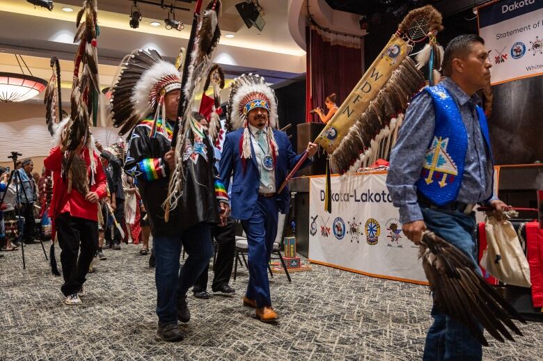 Several men in formal dress and traditional Indigenos headwear.