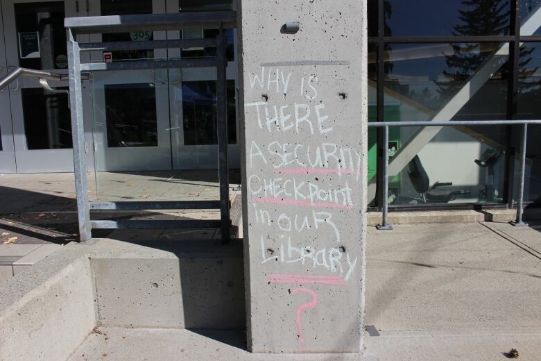 A chalk message that reads, 'Why is there a security checkpoint in our library?'