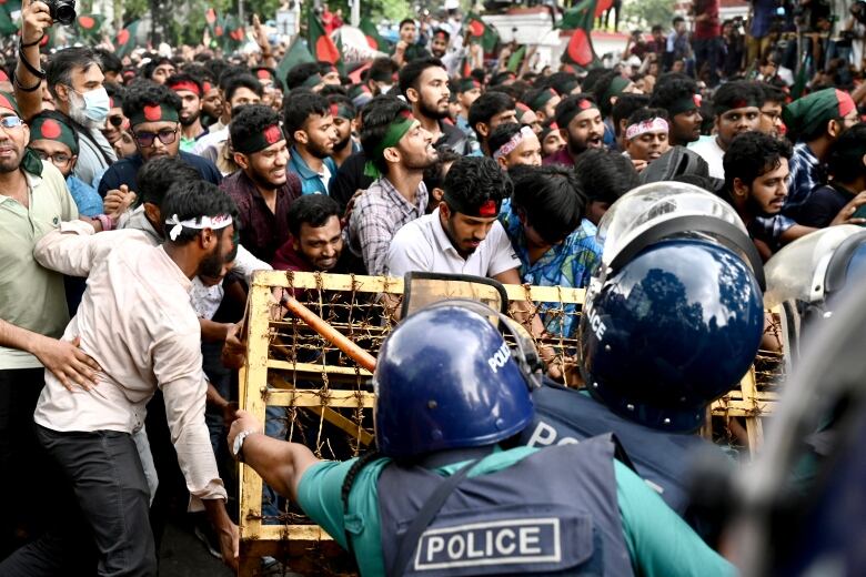 Dozens of men, some wearing headbands are shown trying to move a barricade, with police on the other side of it.