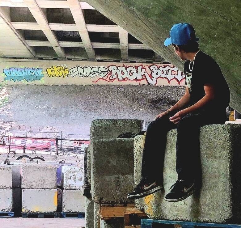 Boy in a blue ball cap sits on a cement block.