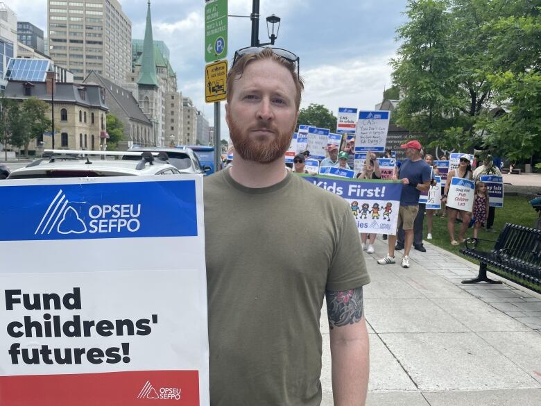 A man holds a sign and is wearing a green shirt.