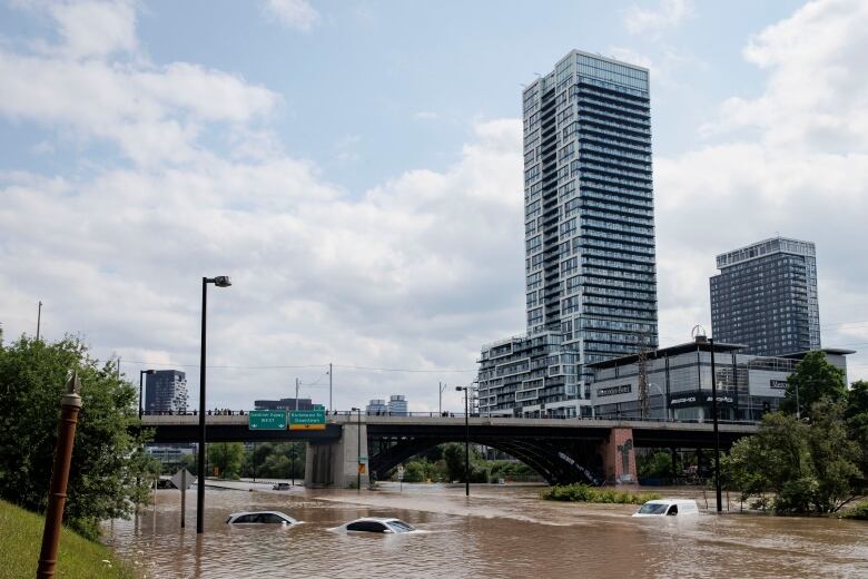 Onlookers take in the spectacle of flooded and abandoned vehicles on the Don Valley Parkway after a major rainfall caused the Don River to burst its banks on July 16, 2024.