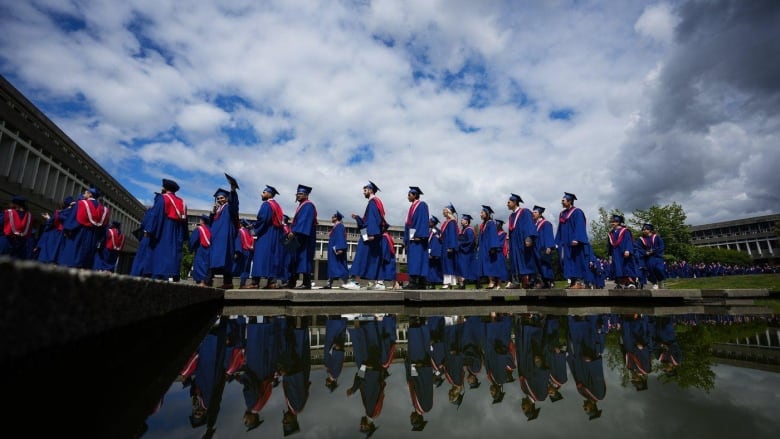 Graduating students are seen walking beside a reflective pond.