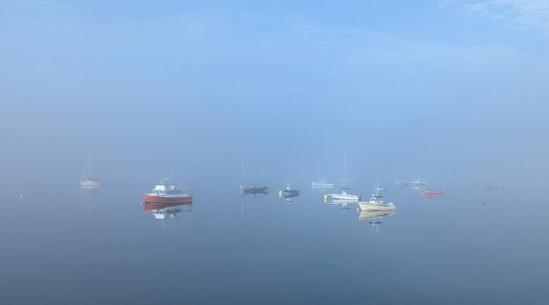 Several boats float on blue, foggy water.