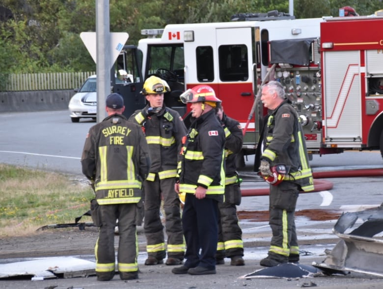 Five firefighters stand on the road amid debris, in front of a fire truck. 