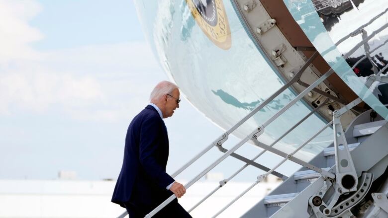 A person holds the railing as they walk up the steps to enter an airplane.