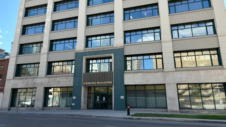 An off-white building with many windows reflecting a clear blue sky. 