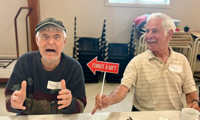 Two older men pictured making faces. One holds up an arrow that reads 