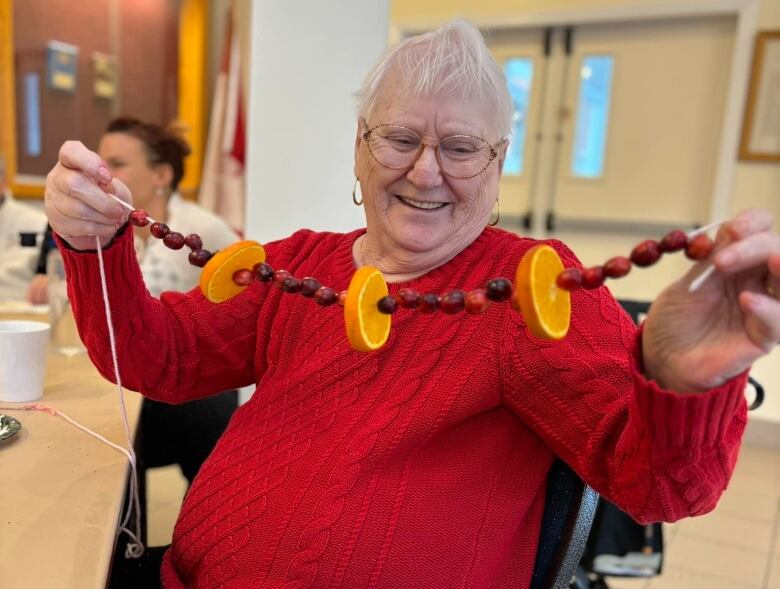 A smiling woman holding up a string of cranberry and orange garland