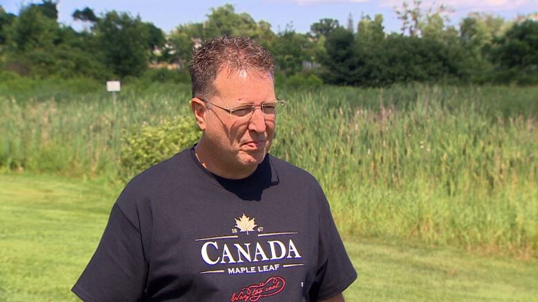 A man with a t-shirt stands on a lawn.