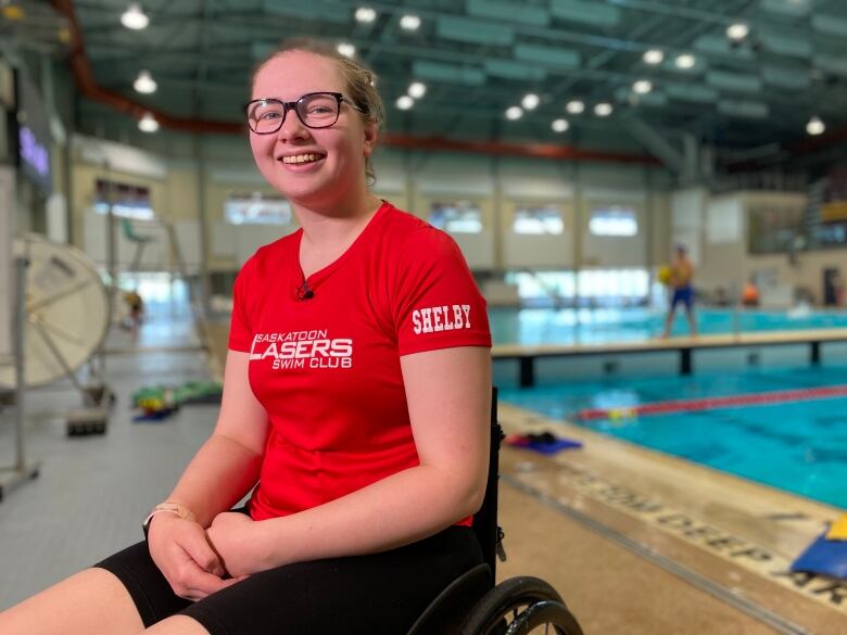 A woman in a red shirt sits in a wheelchair in front of a pool