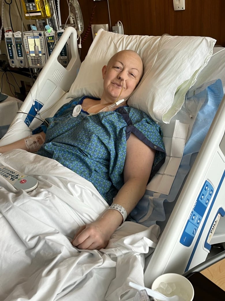 A bald woman lies in a hospital bed. 