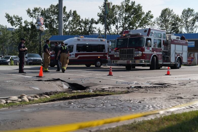 a hole in the road. caution tape is around the hole and firefighters are standing near it.