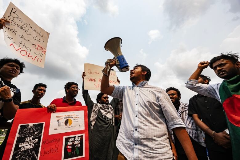 A man screaming through a loudspeaker, surrounded by people holding signs.