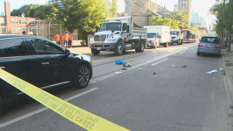 A stopped car on the road, police tape and belongings are strewn on the road.