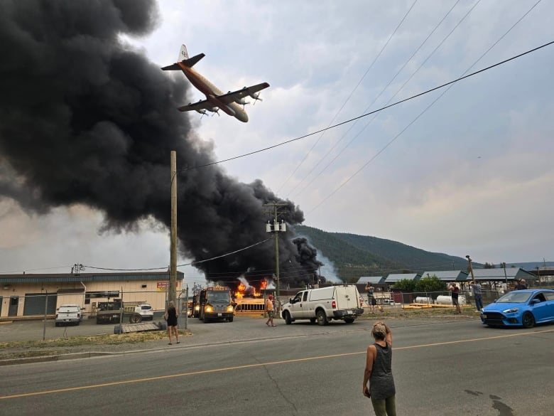 A huge black plume of smoke with an air tanker in the sky.