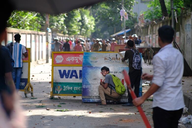 People are seen behind a barricade facing towards another group opposite in the distance. One person is crouched down behind the barricade.