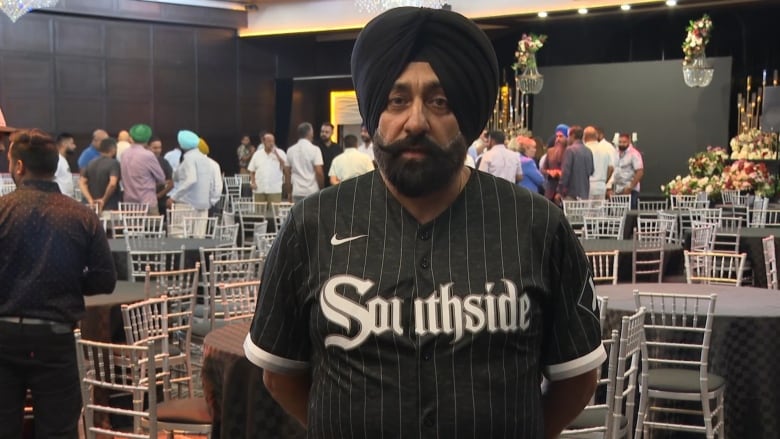 A man in a turban speaks to a camera at a community meeting.