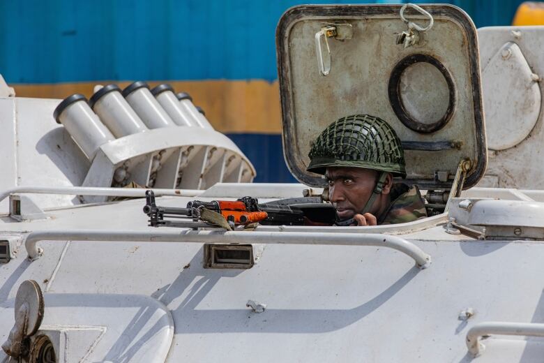 A person's head is visible outside the hatch of an armoured vehicle. They are looking to the left, holding a gun.