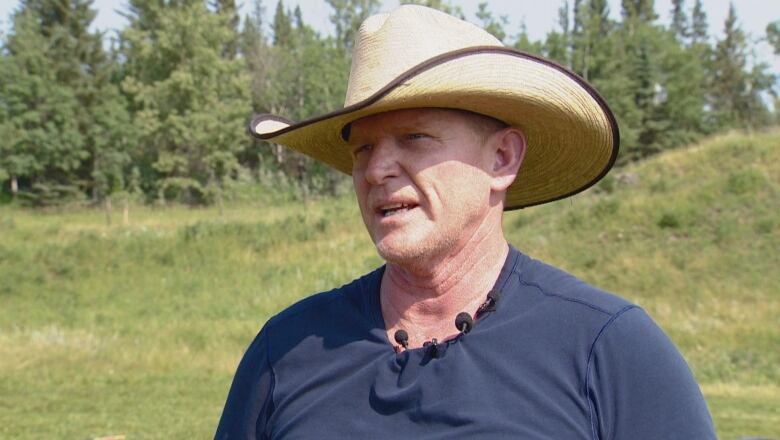 A man in a  dark blue T-shirt is seen wearing a hat.