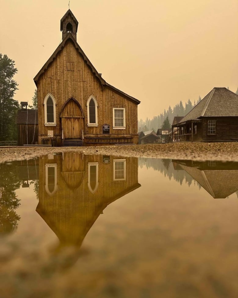 A wooden church is reflected in a puddle of water with a smoky backdrop.