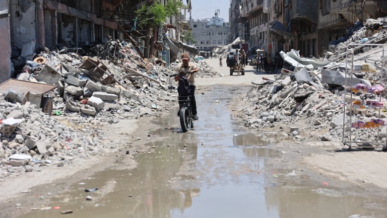 A man rides a bike in rubble.