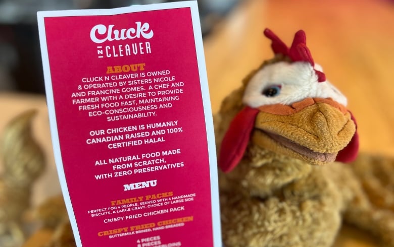 A menu for a chicken restaurant is displayed next to a plush chicken.