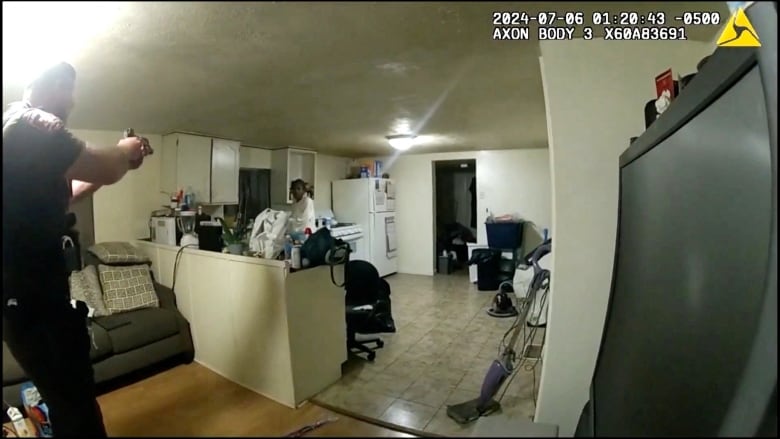 An image taken from bodycam footage shows a police officer aiming  a gun at a person inside a home.