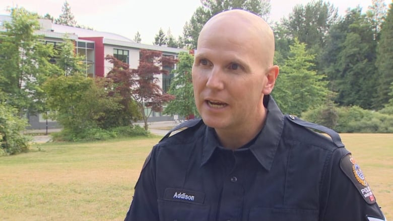 A bald white man in a police uniform speaks in a park.