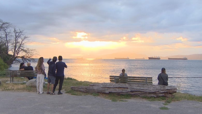 People point and sit on a beach during sunset.